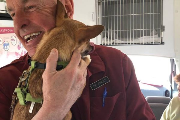 Dr. Ponder smiling and hugging a small brown dog inside of the mobile clinic